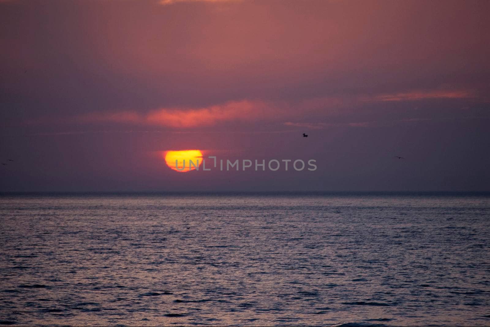 an orange red glowing sunset with layers of cloud over the ocean