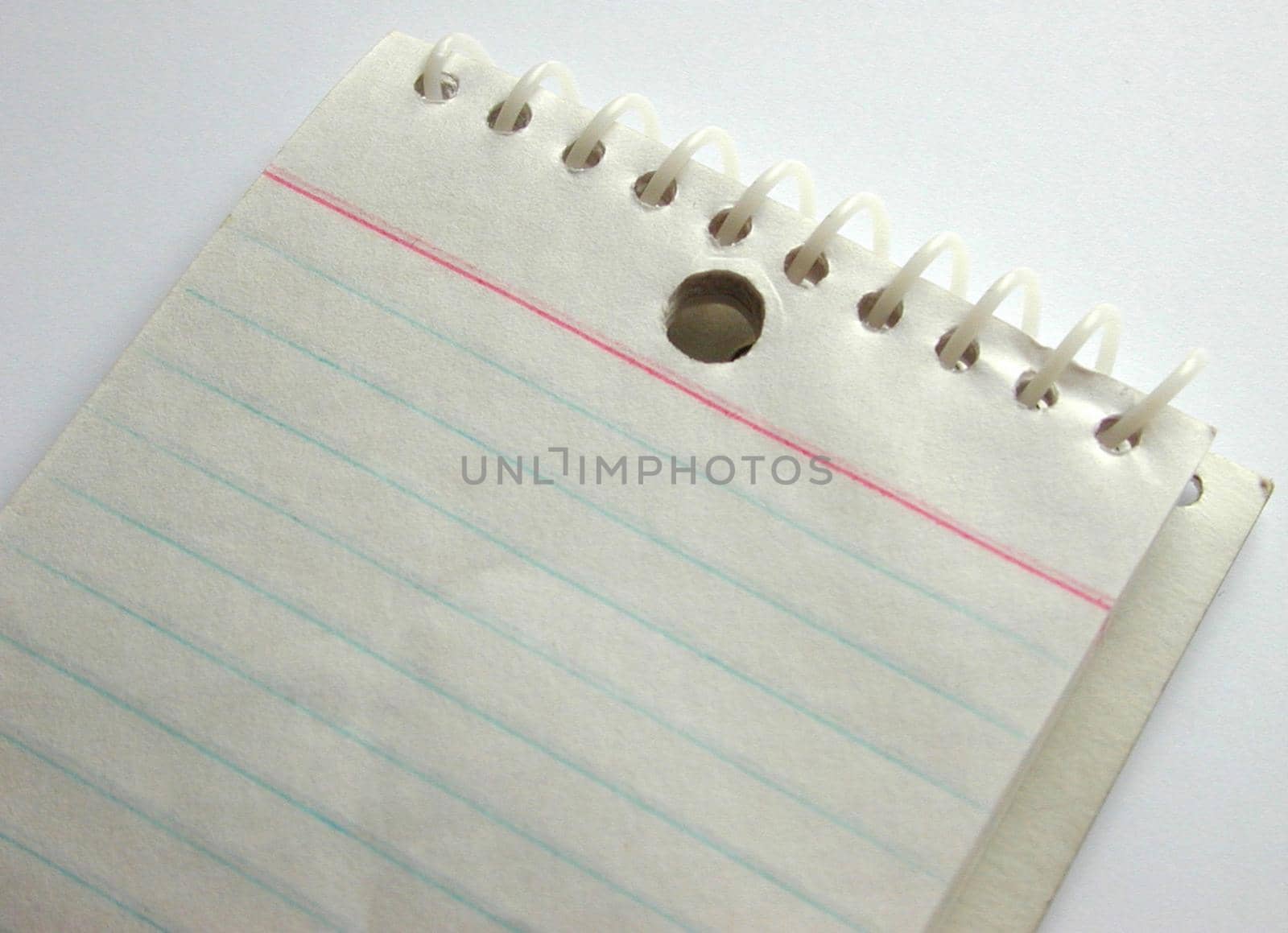 Blank spiral bound notepad with ruled lines on a white background, close up view of a portion of the pad