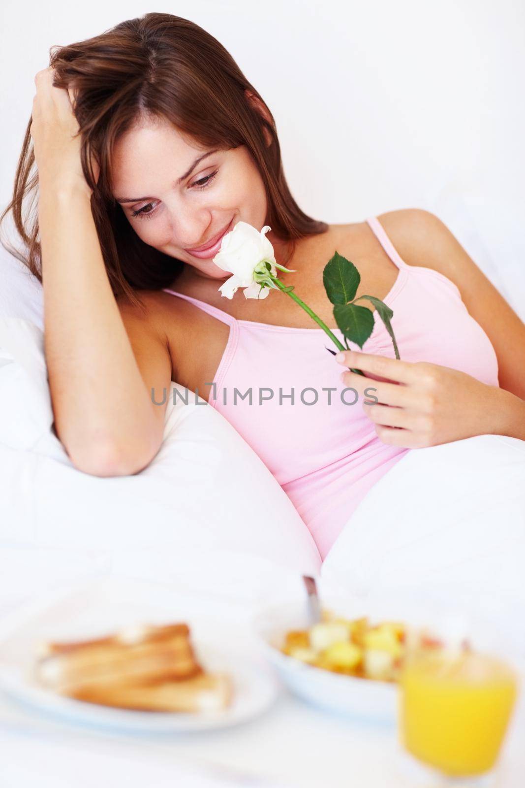 Happy romantic female with breakfast in bed. Cute young female with breakfast and a white rose in bed