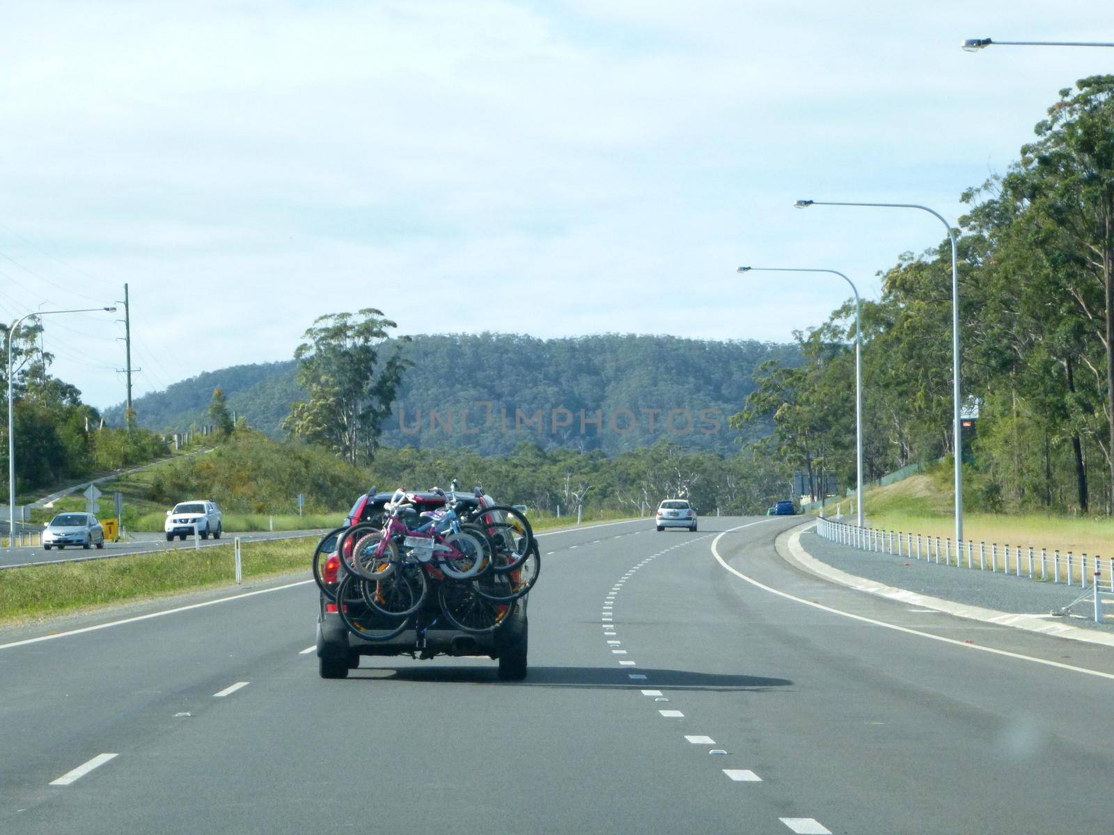Family outing for a day of off road cycling with bicycles of all sizes strapped to a carrier on the back of a car traveling along a freeway