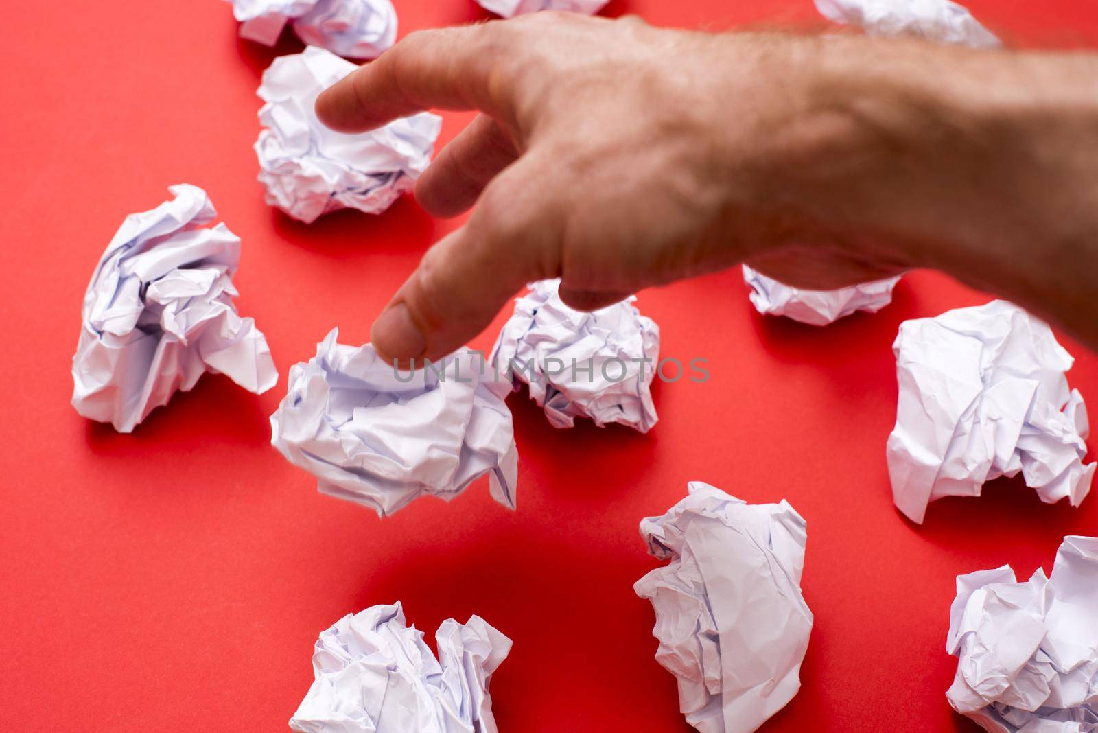 Human hand throwing away balls of paper against red background