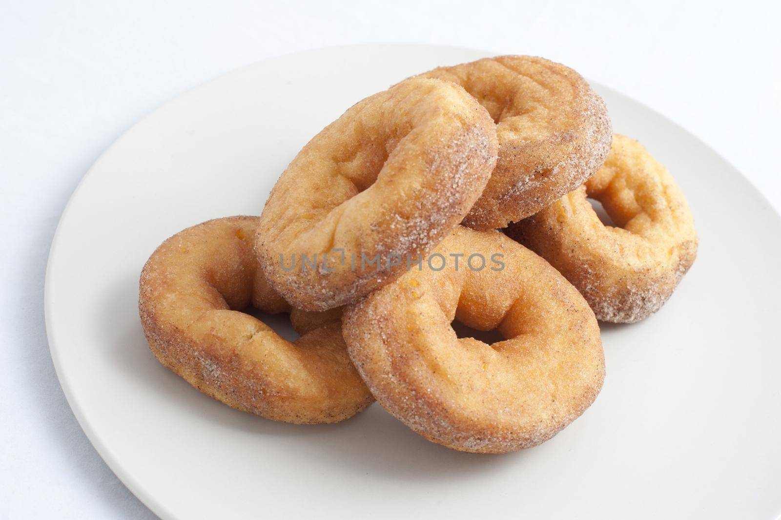 Plate of fresh ring donuts or doughnuts sprinkled with sugar for an unhealthy, but tasty, breakfast