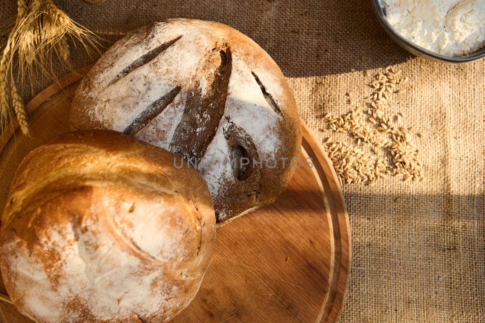 Variety of loaves of fresh baked homemade delicious whole grain multigrain bread on a wooden board on burlap tablecloth by artgf