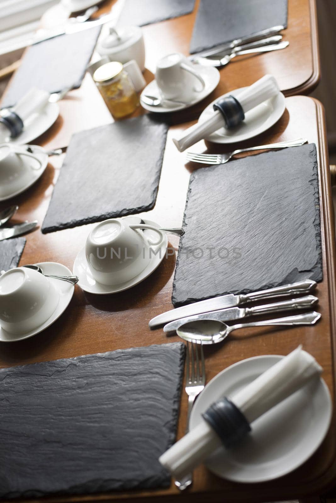 Laid wooden dining table in a restaurant with cutlery, crockery and linen in a close up cropped view of a single place setting