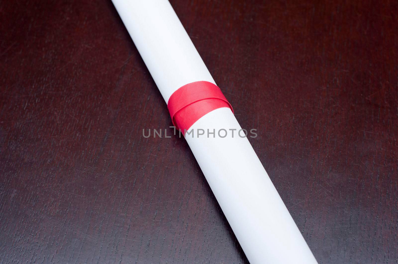 Rolled diploma or certificate neatly tied with a red ribbon on a dark background with copyspace conceptual of educational achievement
