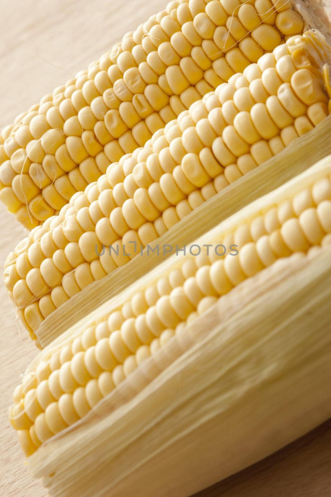 Three fresh uncooked dehusked sweet corn on the cob ready to be prepared for a delicious snack or vegetable accompaniment to a meal, close up view in an oblique row