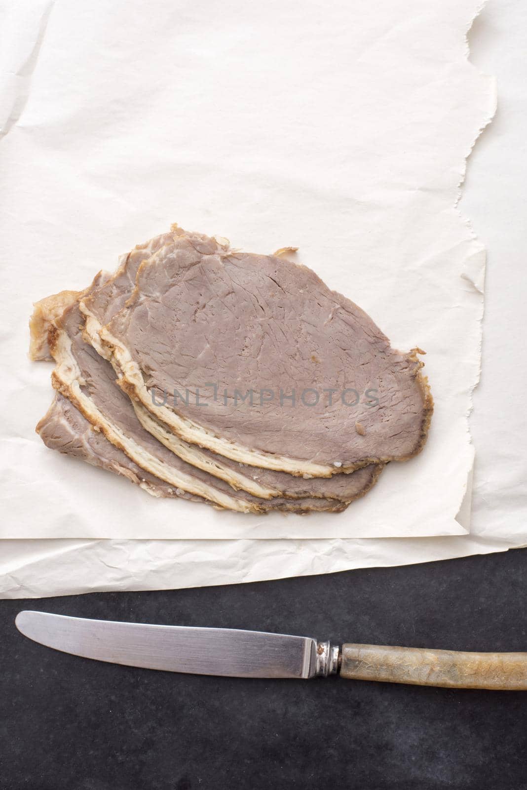 A close up of sliced roast beef and knife on butchers paper.