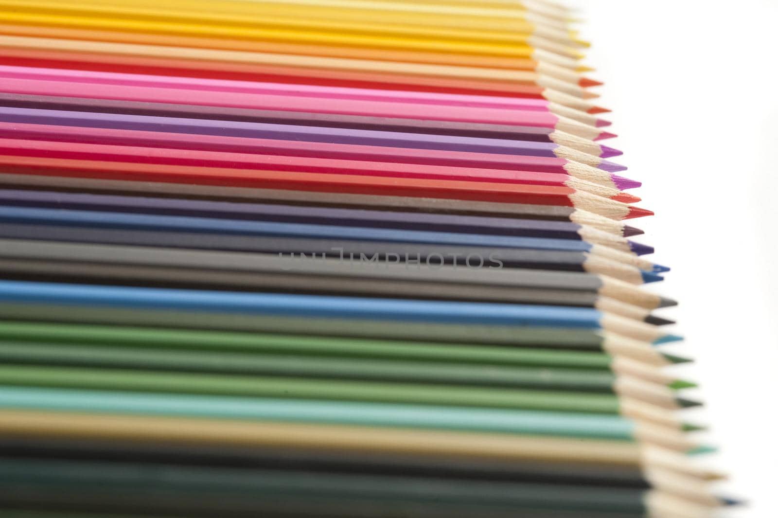 Large set of colored pencil crayons arranged in a neat receding line viewed low angle with selective focus to the red shades