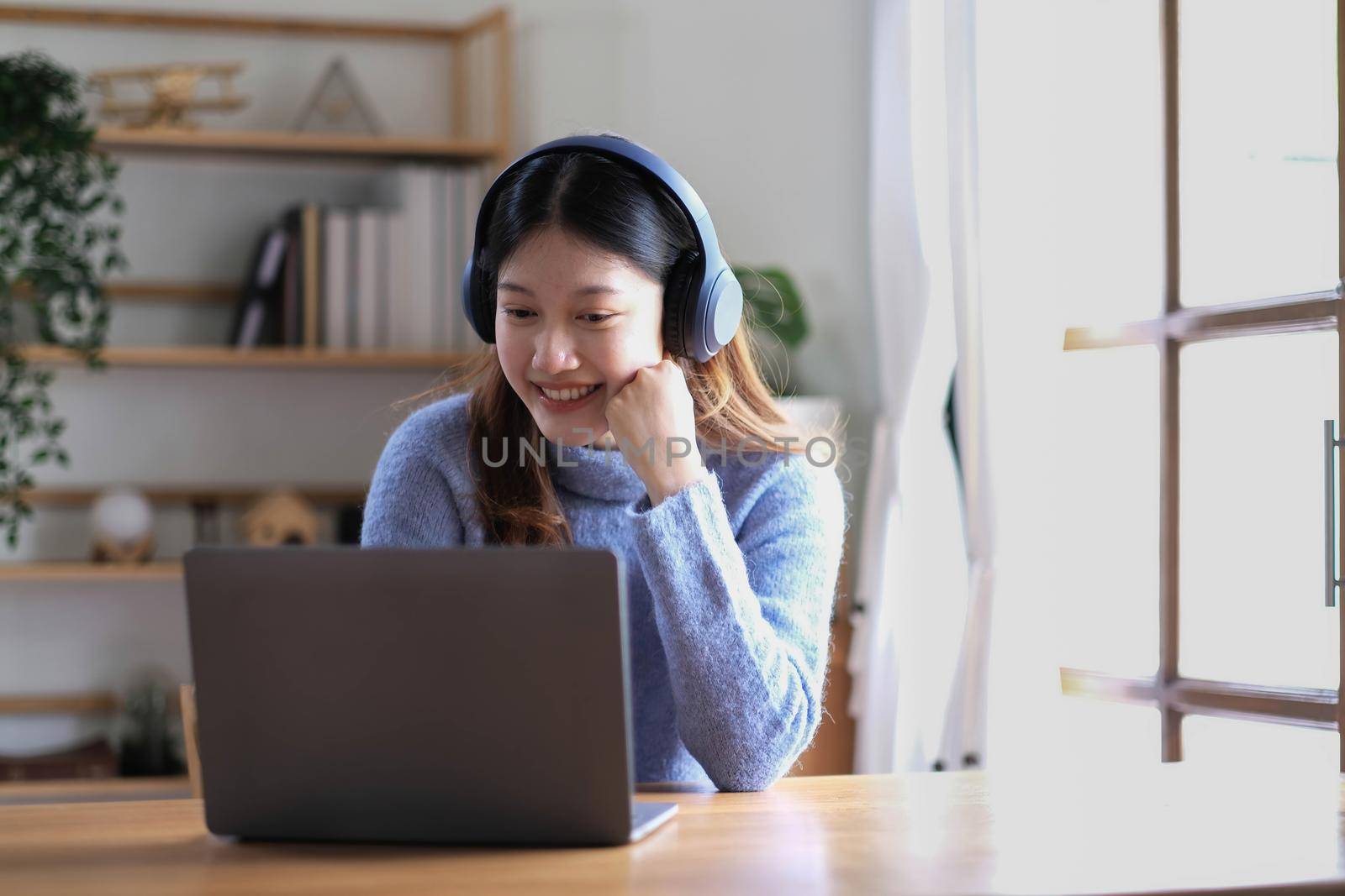 Cheerful beautiful Asian woman wearing headphones and look to digital tablet at video calling meeting and study online on the Internet. by wichayada