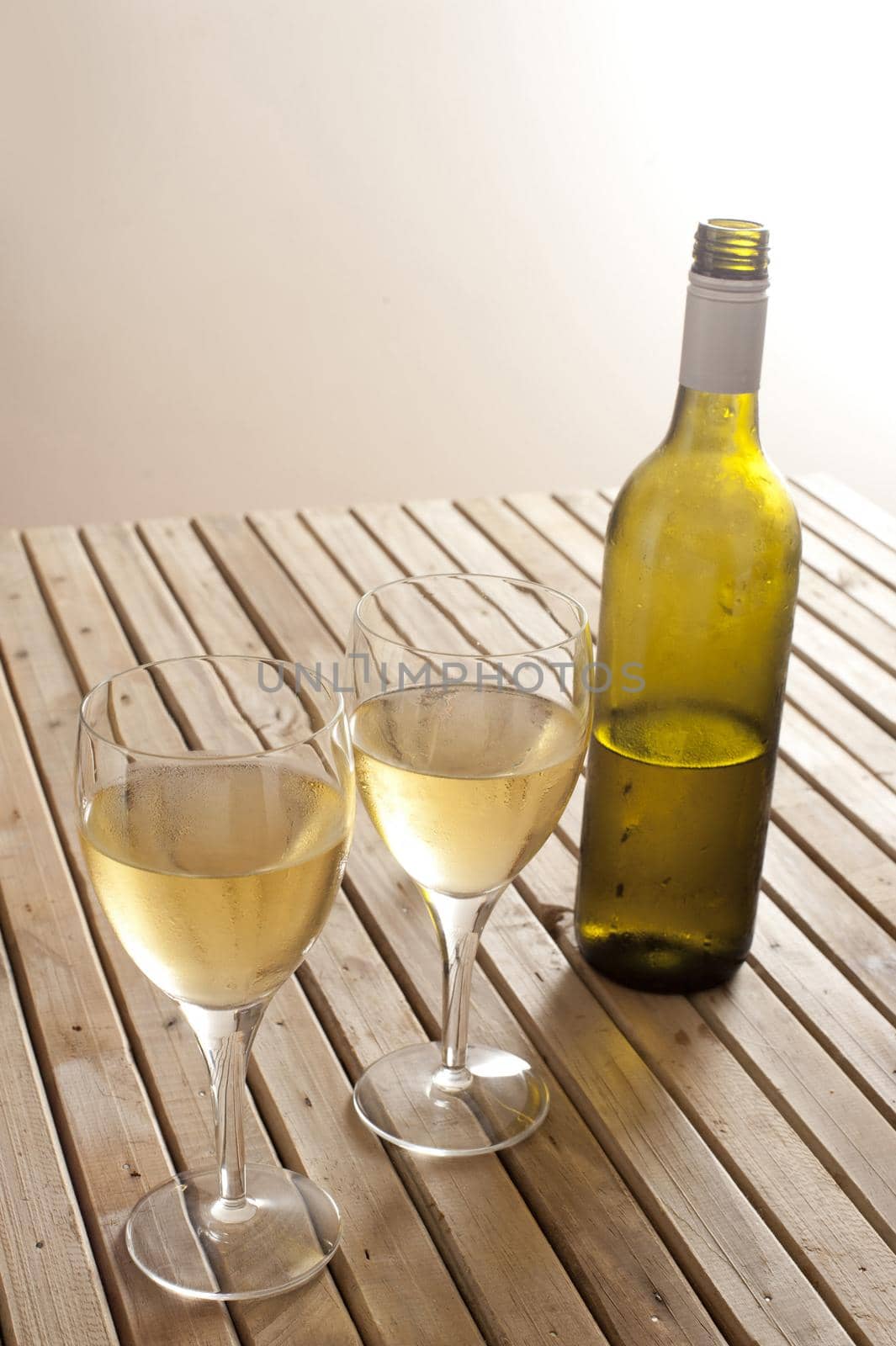 Open unlabelled white wine bottle with two full glasses of wine on a slatted wooden table with copyspace
