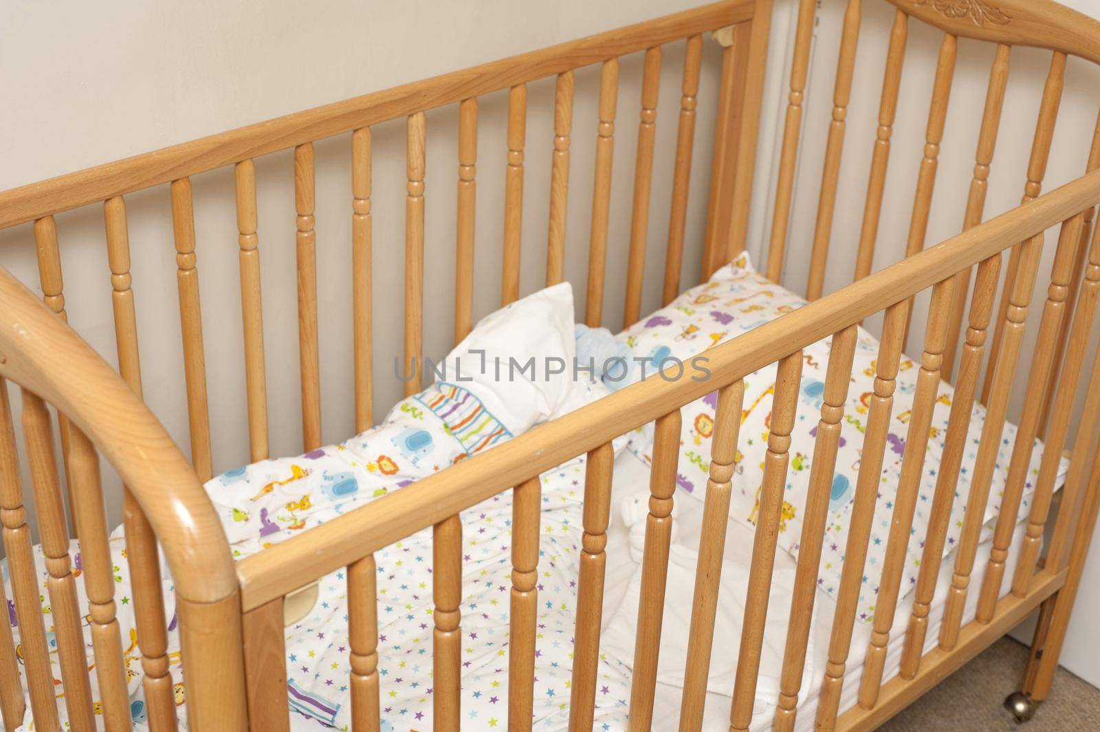 Empty wooden baby cot or crib with colorful pattern linen in the corner of a romom, close up view