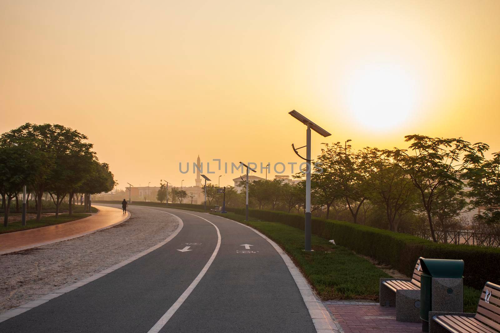 Jogging and cycling tracks in Al Warqa park, Dubai, UAE early in the morning. Lamp post powered by solar panels can be seen in the picture as well as minaret of a mosque. Outdoors
