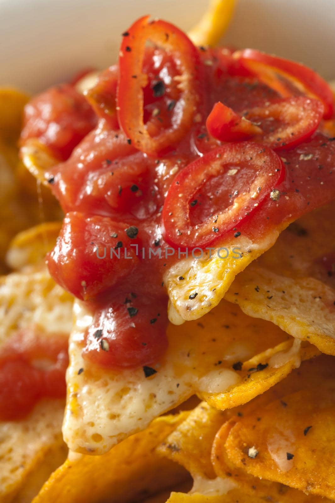 Topping of hot chili pepper and tomato salsa on corn tortilla chips with melted cheese for a tasty Tex-Mex or Mexican snack