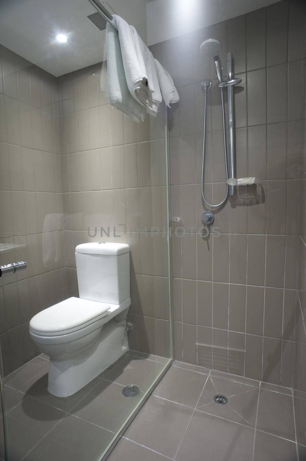 White ceramic toilet fixture and shower in a small bathroom with neutral beige decor and clean white towels