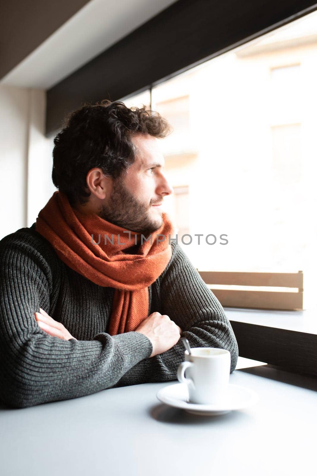 Pensive young man looking out the window, enjoying early morning in coffee shop. Vertical image. Lifestyle.
