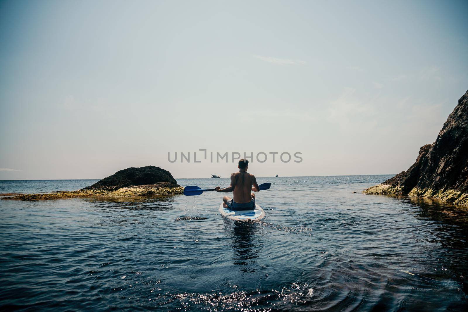 Side view foto of a man swiming and relaxing on the sup board. Sportive man in the sea on the Stand Up Paddle Board SUP. The concept of an active and healthy life in harmony with nature