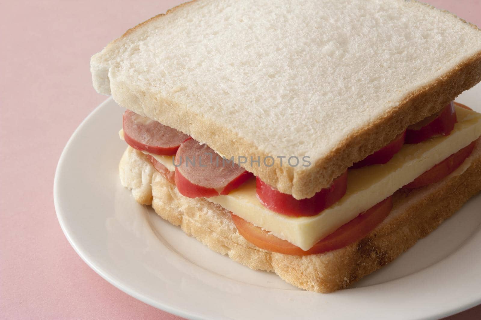 Tasty sandwich using plain white bread with cheese and sausage bits atop sliced tomatos