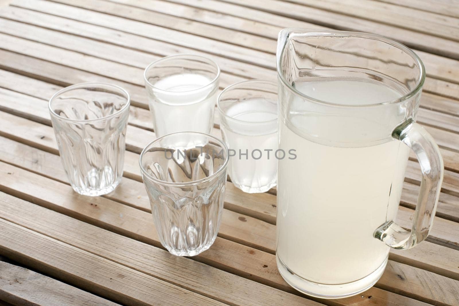 Fresh homemade lemonade in a jug sitting on wooden picnic table with two full and two empty glasses for a refreshing summer drink