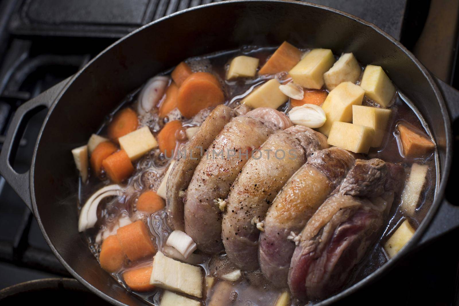 A close up of a trussed, beef shoulder simmering in a pot with assorted vegetables.