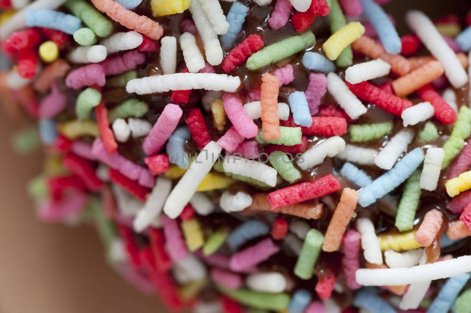 Background texture of multicolored sprinkles on a chocolate glazed doughnut