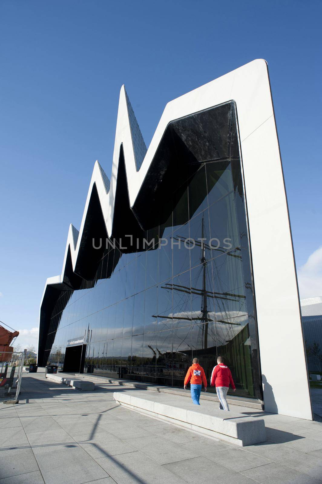 Distinctive modern exterior facade of the Riverside Museum, Glasgow. Scotland with its zigzag design and large window reflecting a tall ship in the harbour