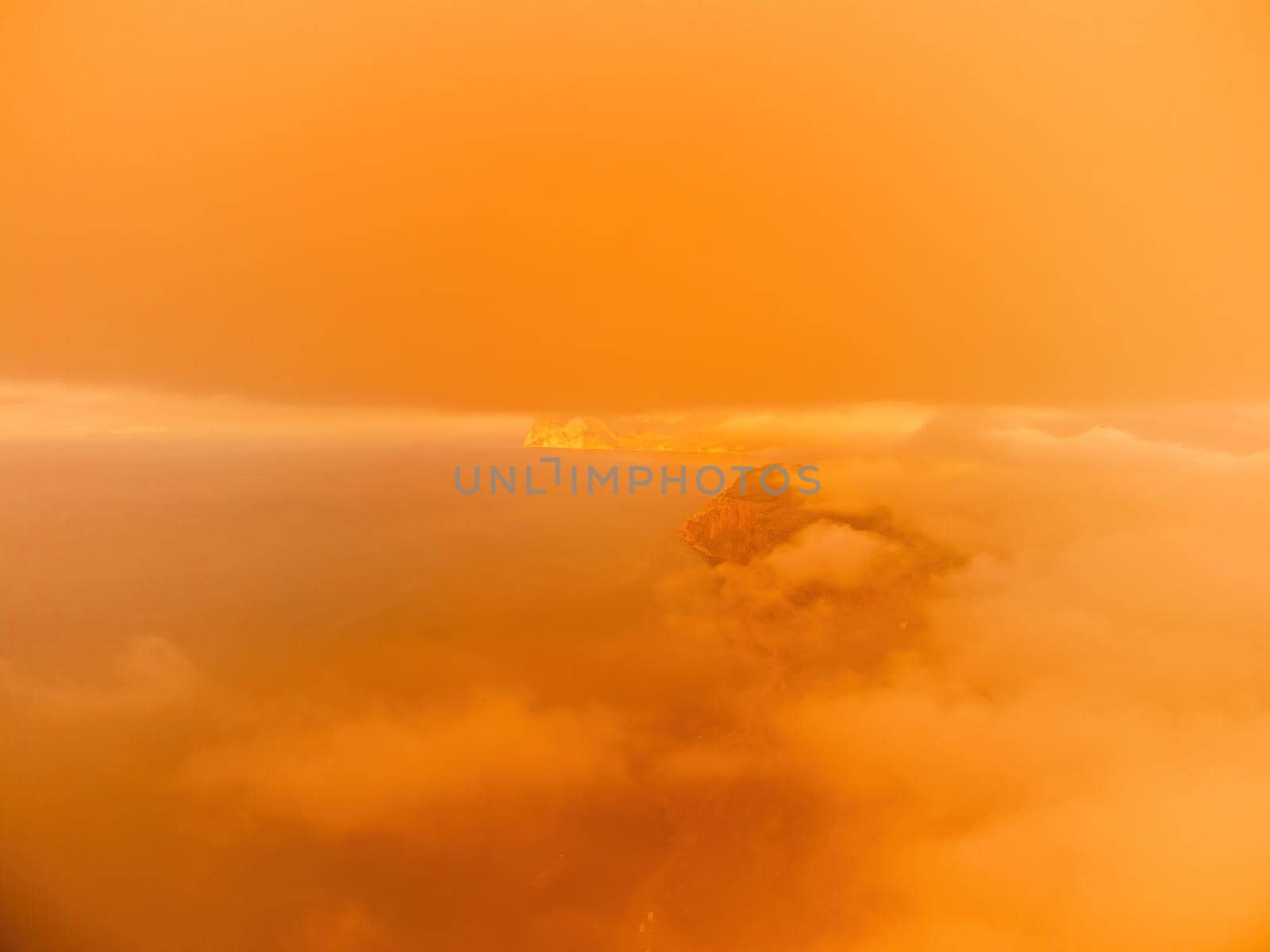 A red burning sunset over the sea with rocky volcanic cliff. Abstract nature summer or spring ocean sea background. Small waves on golden warm water surface with bokeh lights from sun. by panophotograph