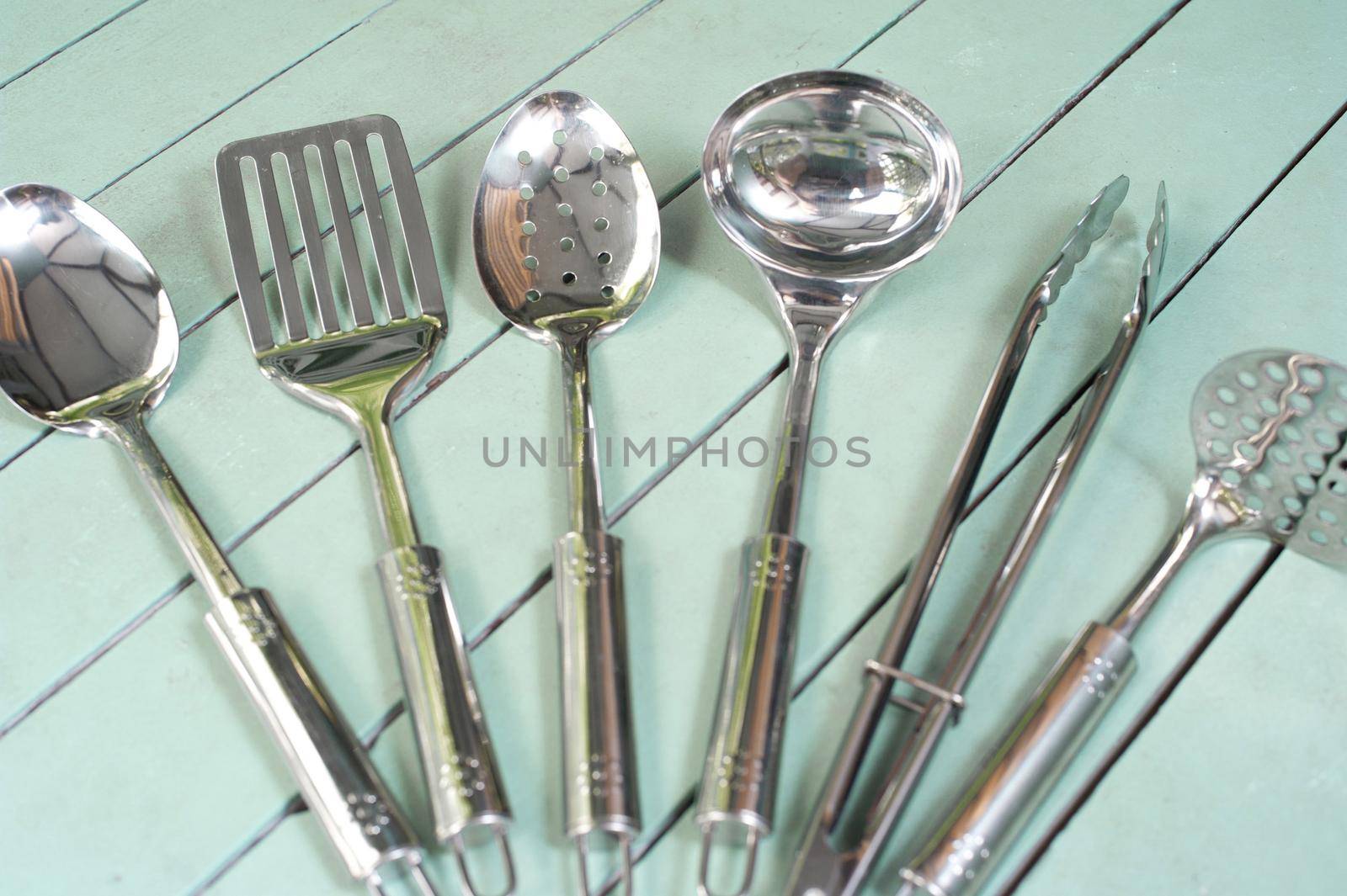 Set of clean stainless steel kitchen utensils displayed fanned out on a rustic green slatted table