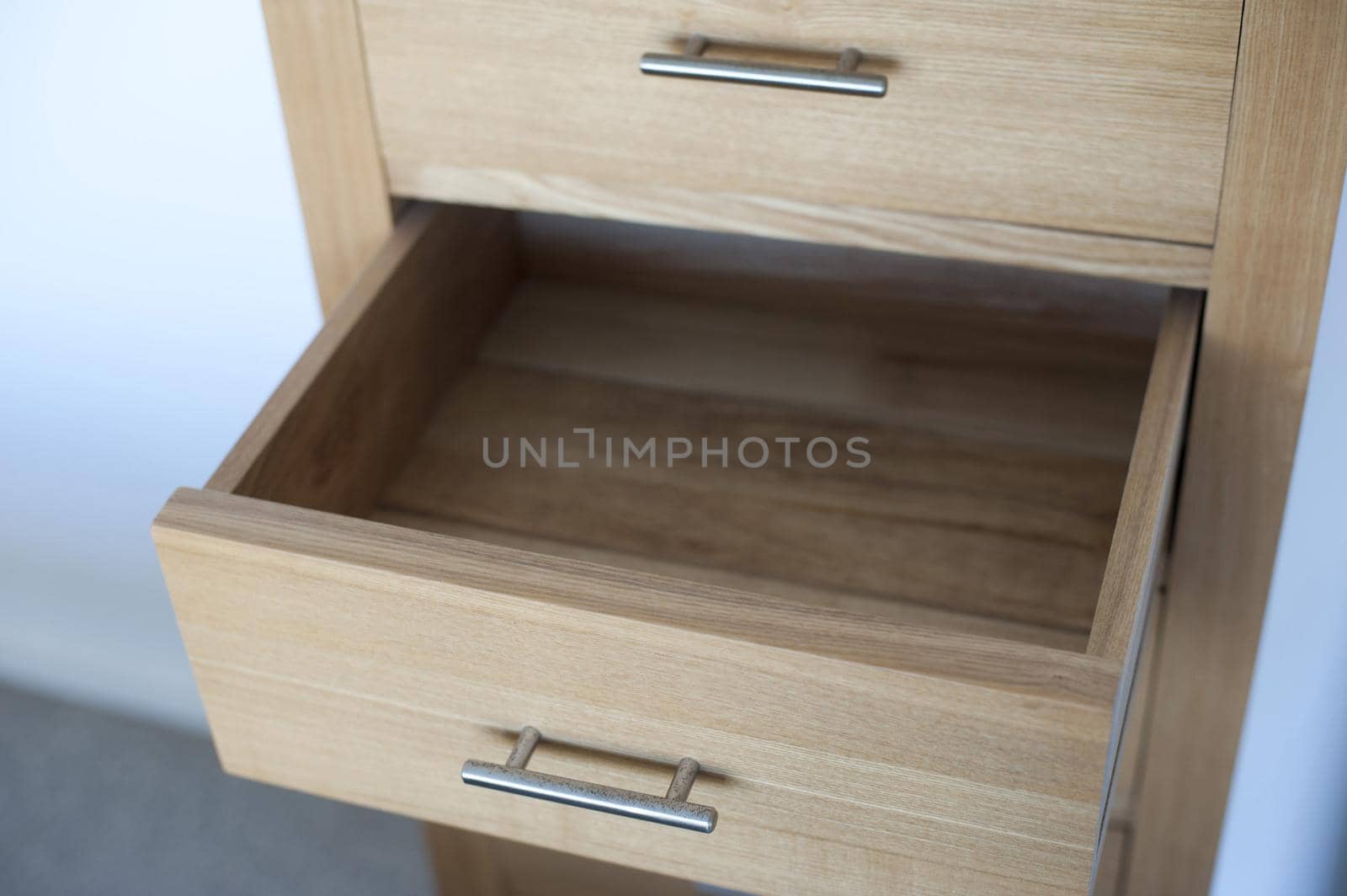 High angle view of an empty open wooden drawer in a small natural wood cabinet against a white indoor wall