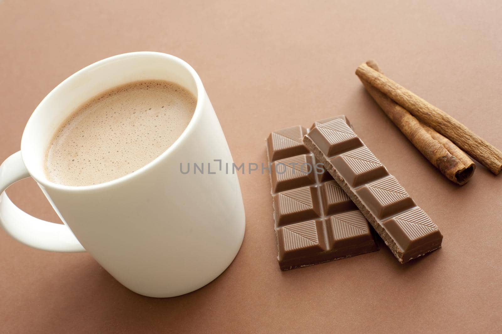 Delicious mug of hot cinnamon chocolate drink for a cold winter day with stick cinnamon and a partial bar of chocolate lying alongside