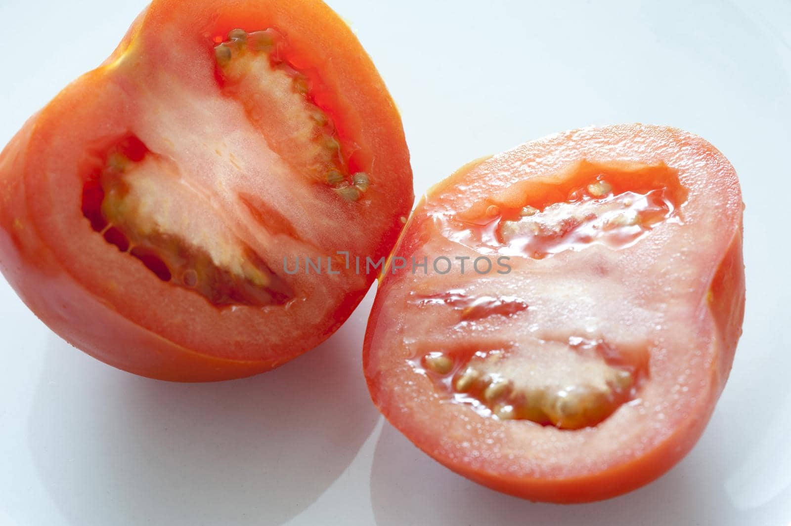 Halved fresh ripe tomato displayed to show the juicy pulp over a light grey background