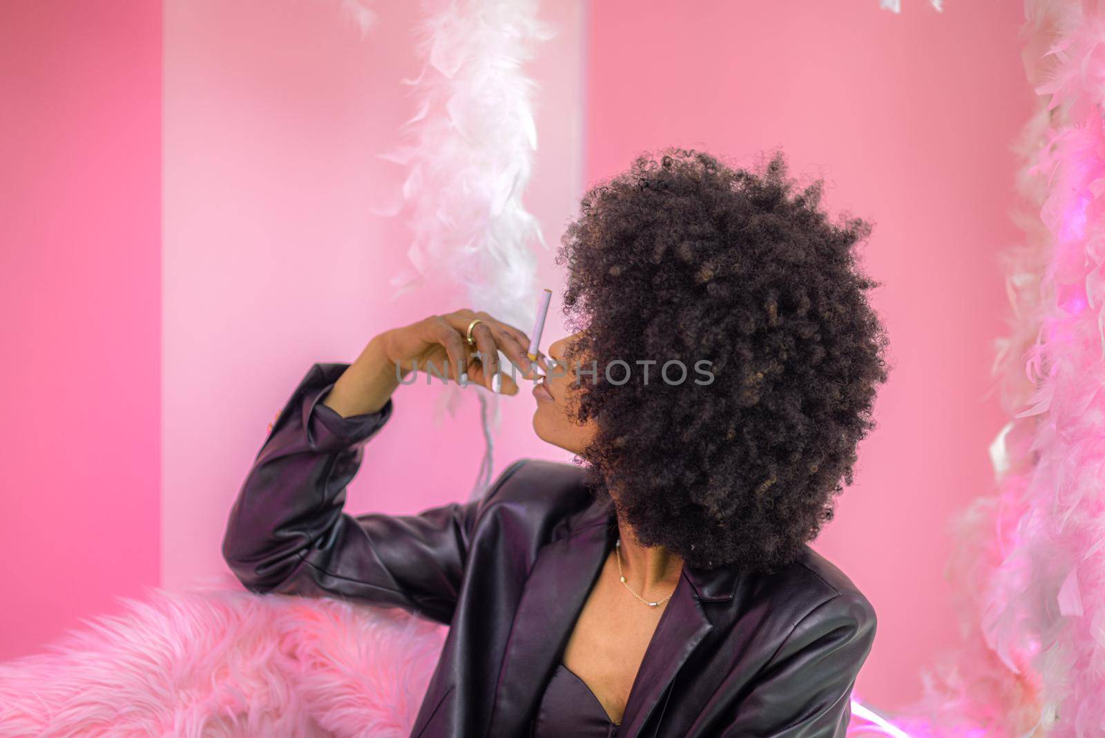 Young attractive African woman with happy cheerful smile smoking in studio