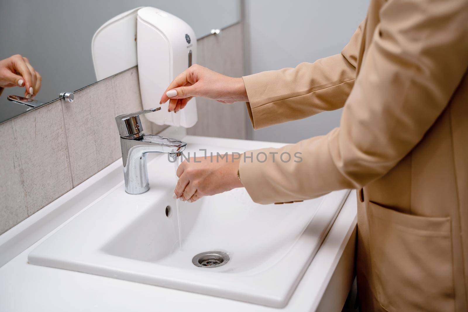 A woman washes her hands under running tap water in a public toilet