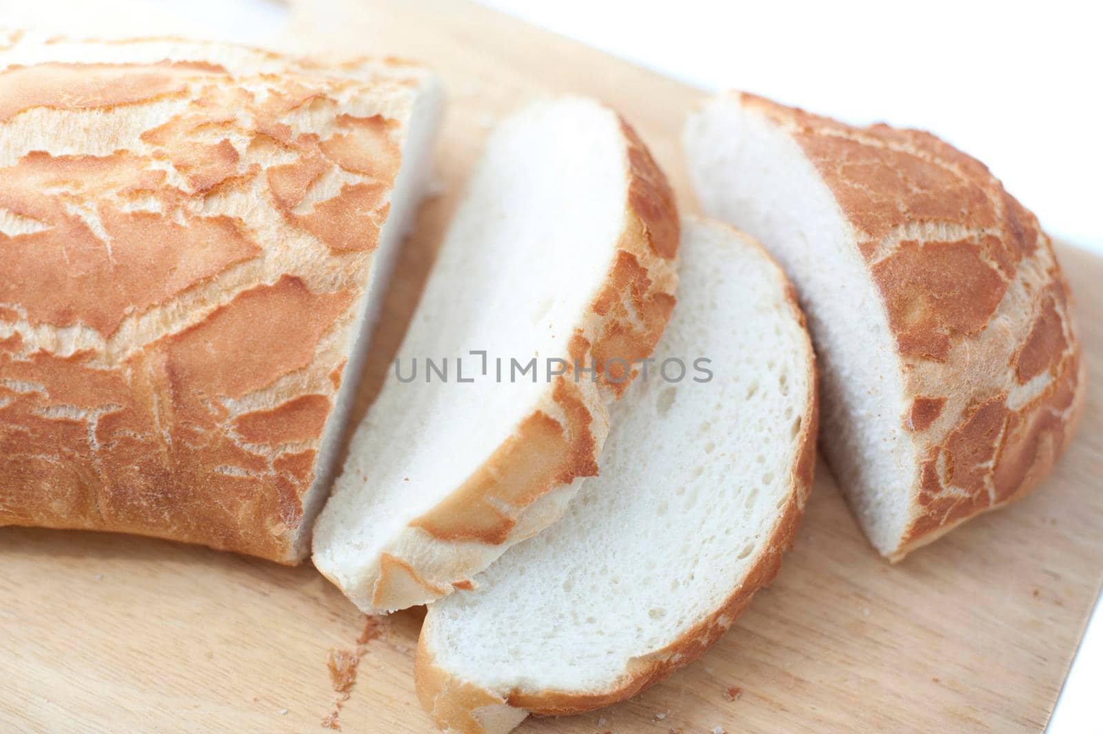 Sliced fresh white crusty bread loaf on a wooden bread board over a white background