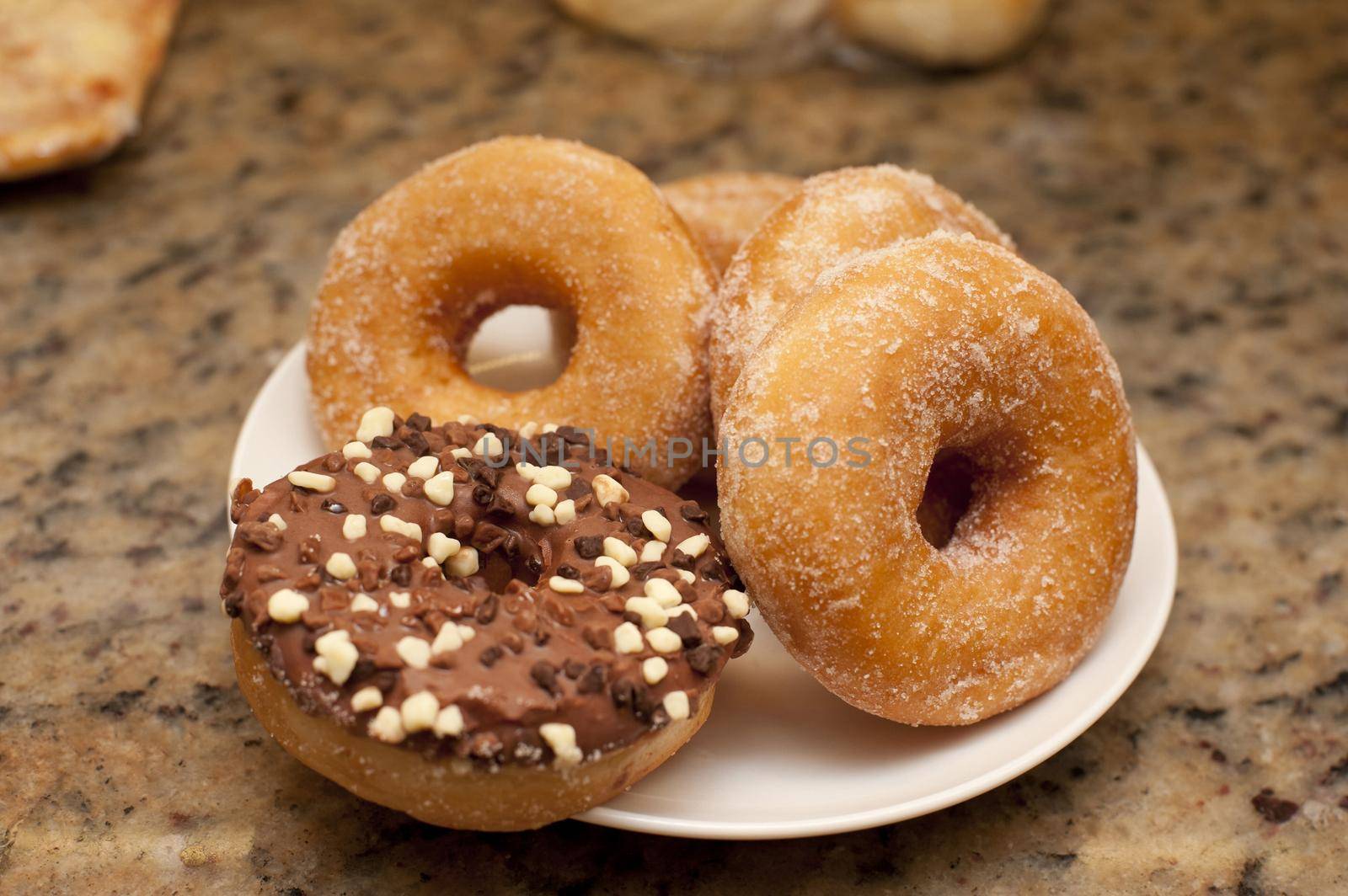 Plate of assorted ring doughnuts with sugared and chocolate glazed donuts ready for a tasty breakfast or teatime