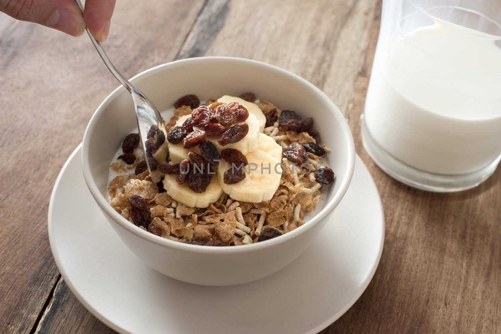 Eating healthy muesli topped with fresh sliced bananas and raisins for breakfast with a jug of milk to the side