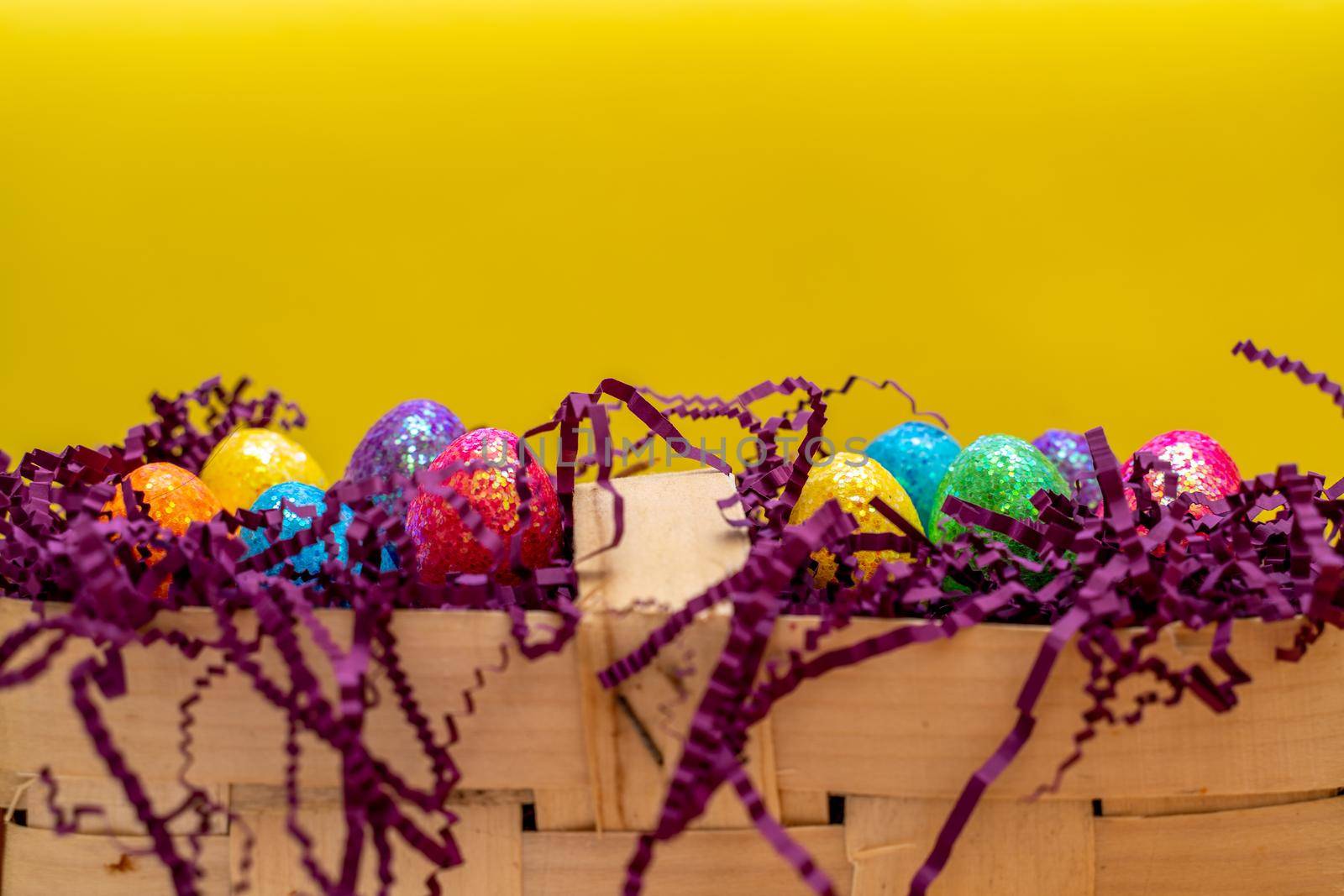 Easter composition from a basket and colored eggs prepared for the holiday on a yellow background.