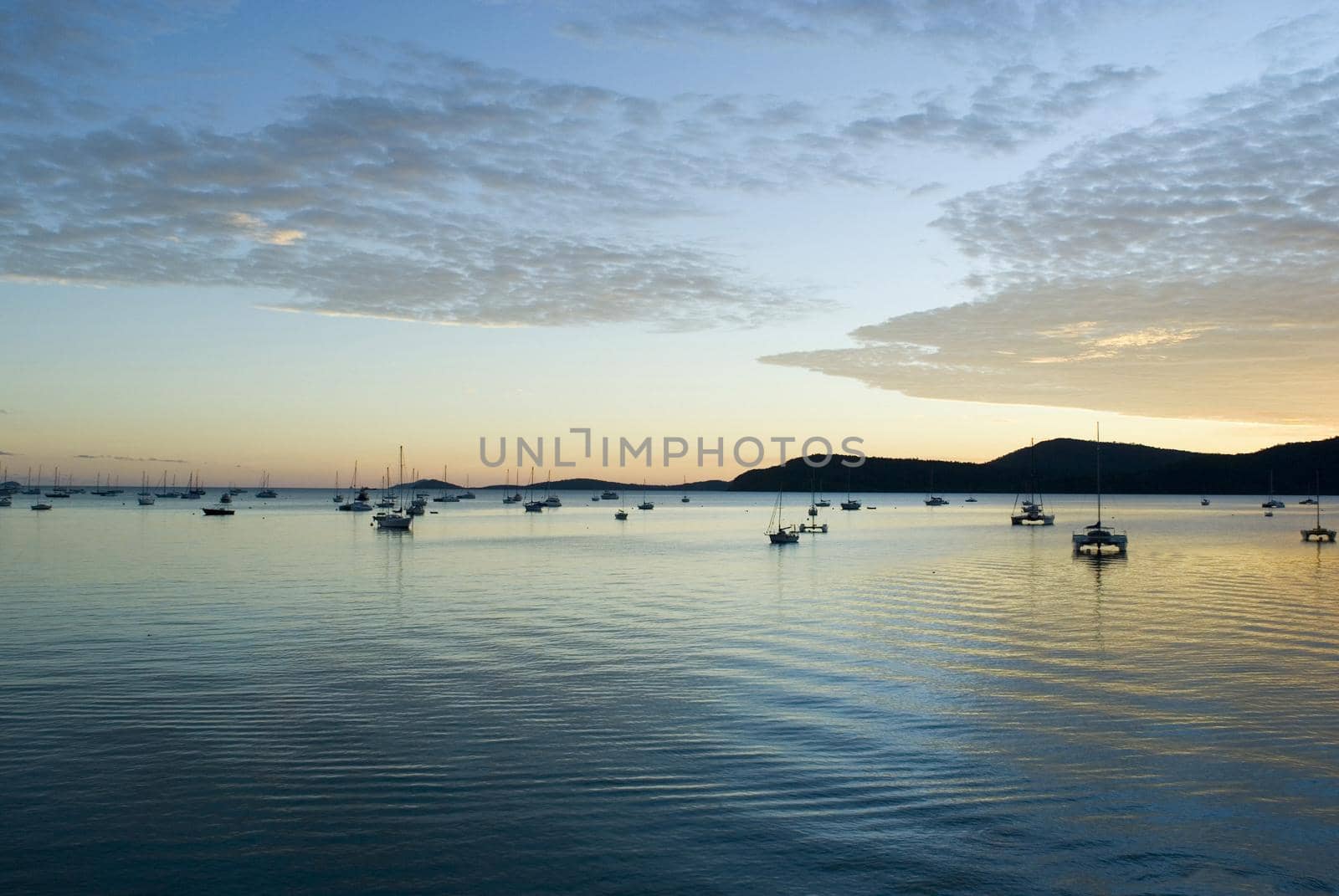 serenity of a still sunset over the water, yachts moored as the sun dissappears below the horizon