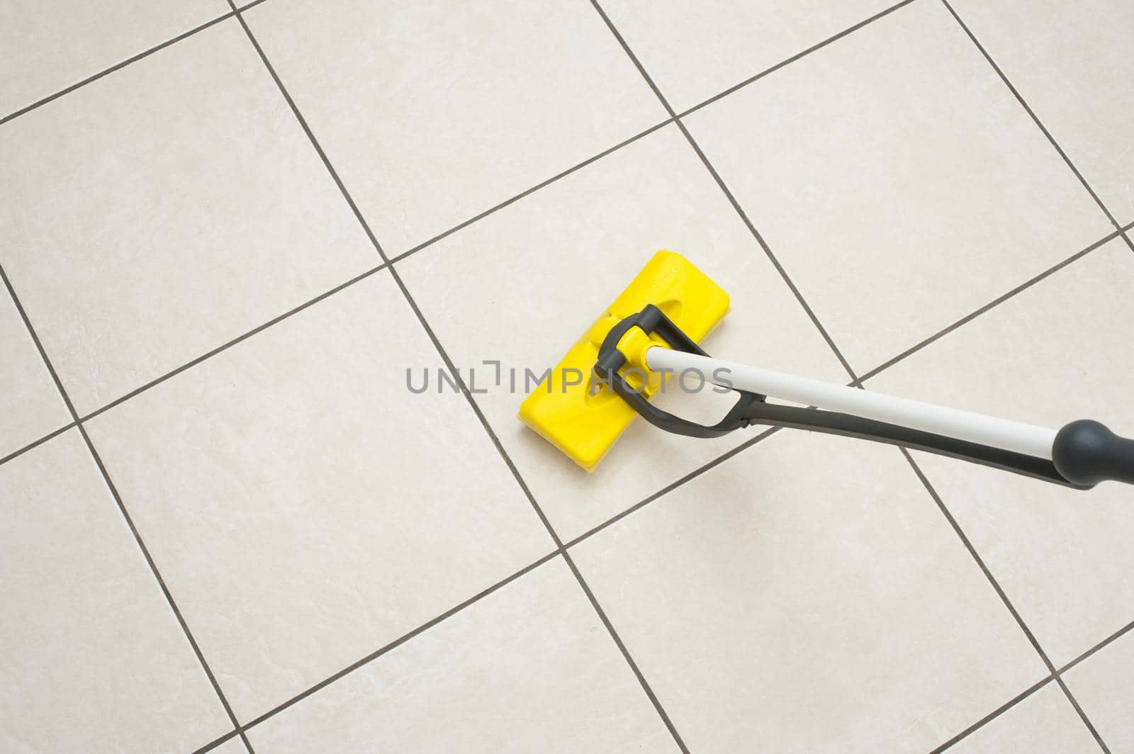 Mopping a tiled white floor with a modern squeegee plastic mop in a household hygiene concept