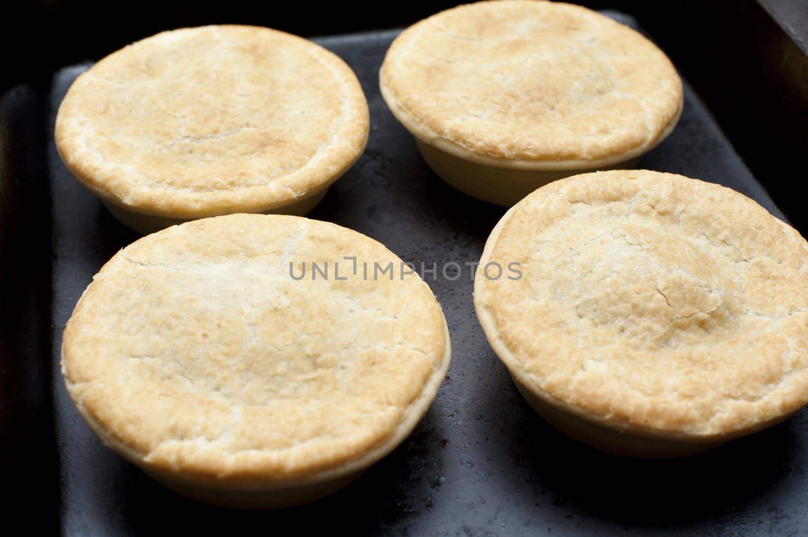 Four freshly baked meat pies topped with a golden crust in a bakery or takeaway restaurant for a quick delicious snack