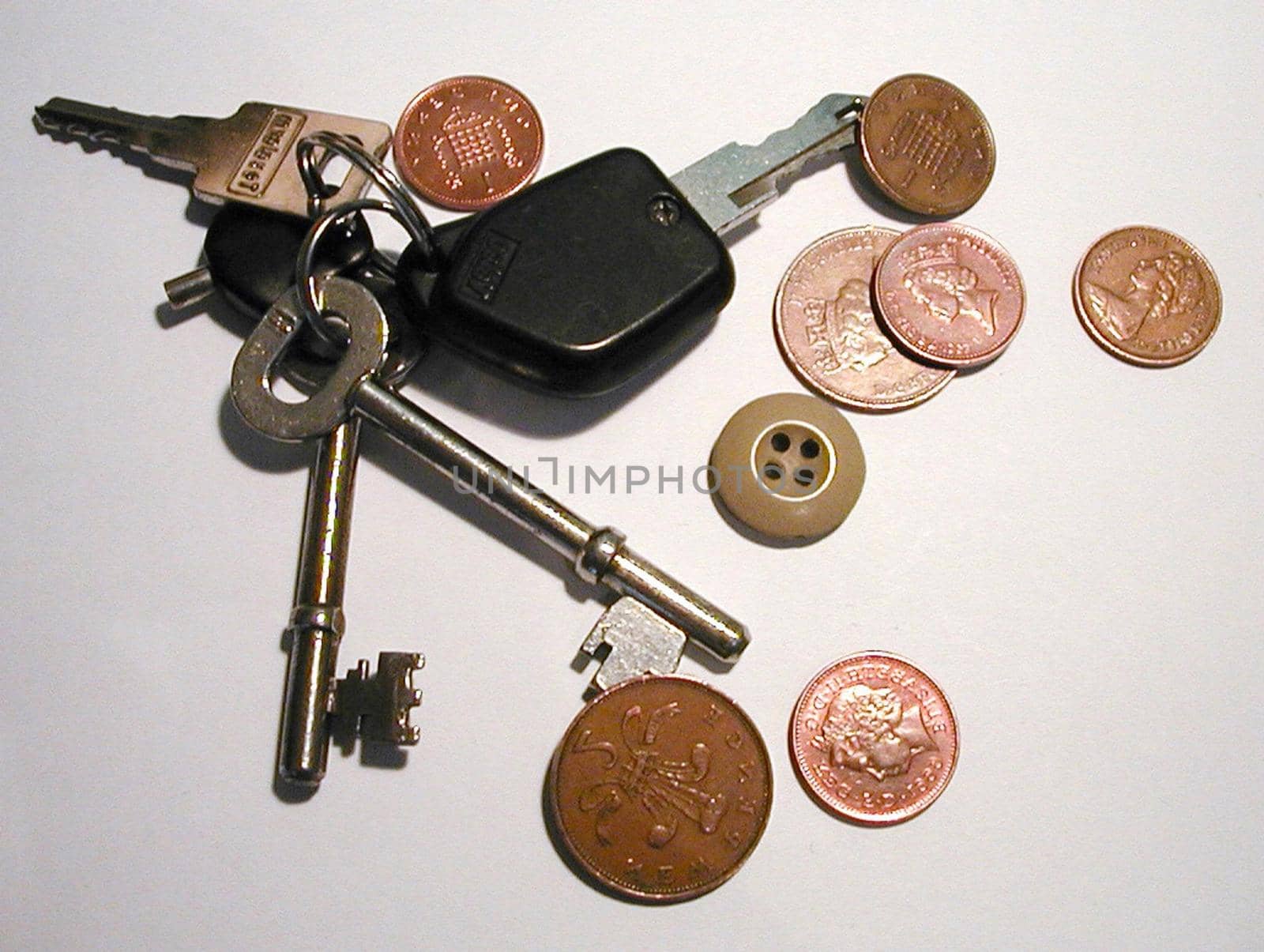 A bunch of house and car keys with scattered coins and a single brown button lying in random array on a grey surface