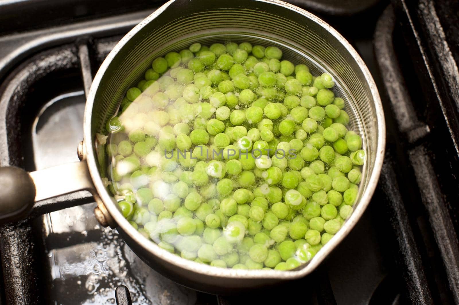 Pot of fresh green peas on the hob standing in water waiting to be cooked and boiled as an accompaniment to a meal