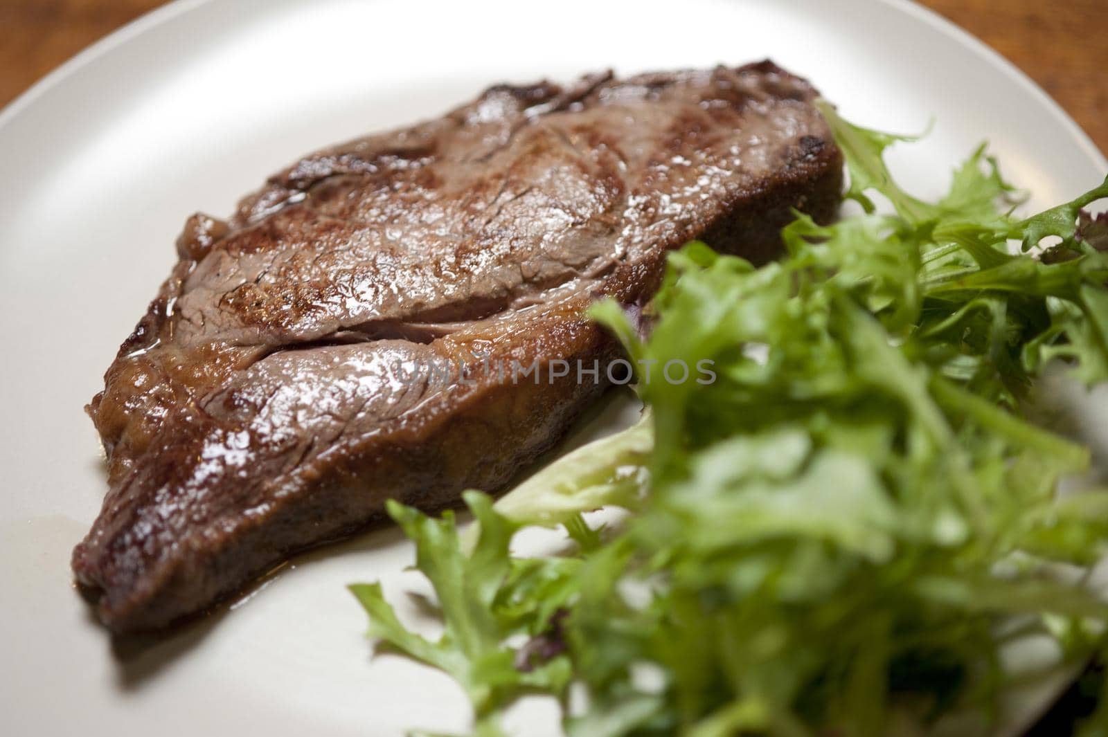 Low angle view of a juicy grilled sirloin steak plated with fresh leafy green salad on a white plate