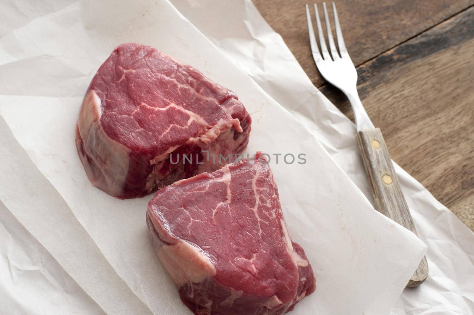 Two juicy thick tender raw medallions of beef fillet steak on greaseproof paper waiting to be prepared for dinner