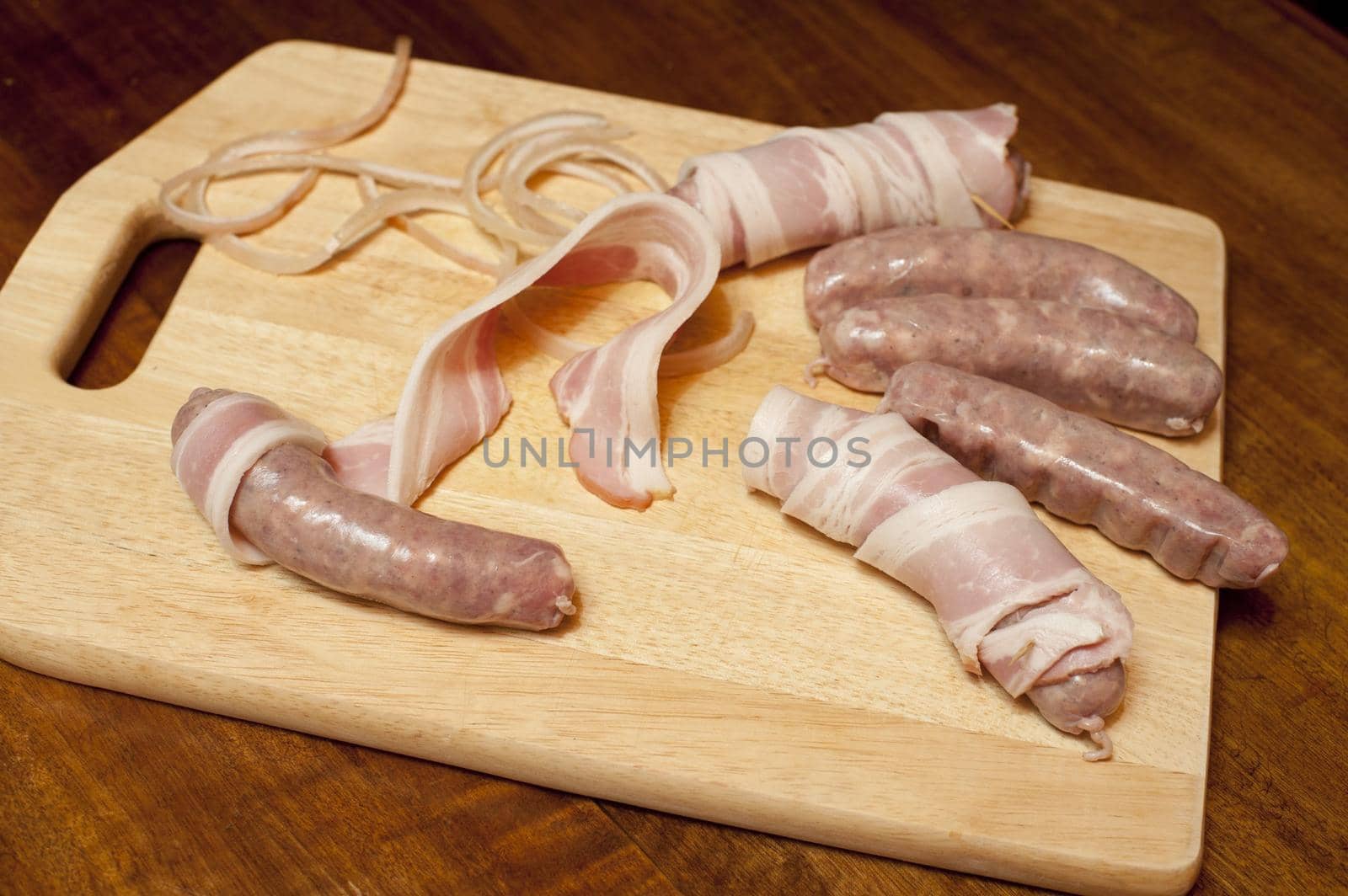 Making bacon rolls with spicy sausages wrapped in rashers of cured bacon laid out on a wooden board in the kitchen