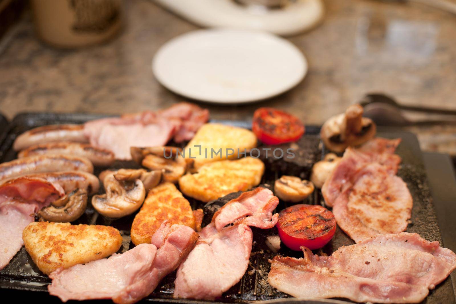 Cooking a hearty English breakfast on a griddle with tomato, bacon, French toast and sausages