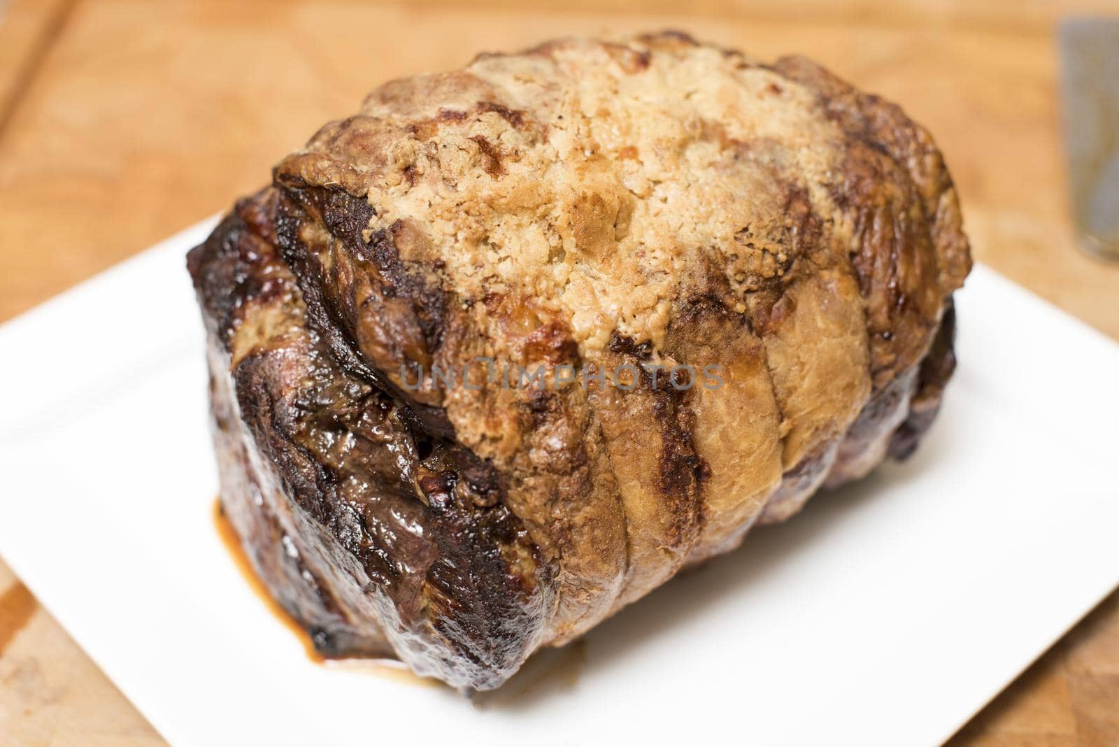 Roast joint of beef fresh from the oven placed on a white square ceramic plate ready to be carved for dinner in a close up high angle view