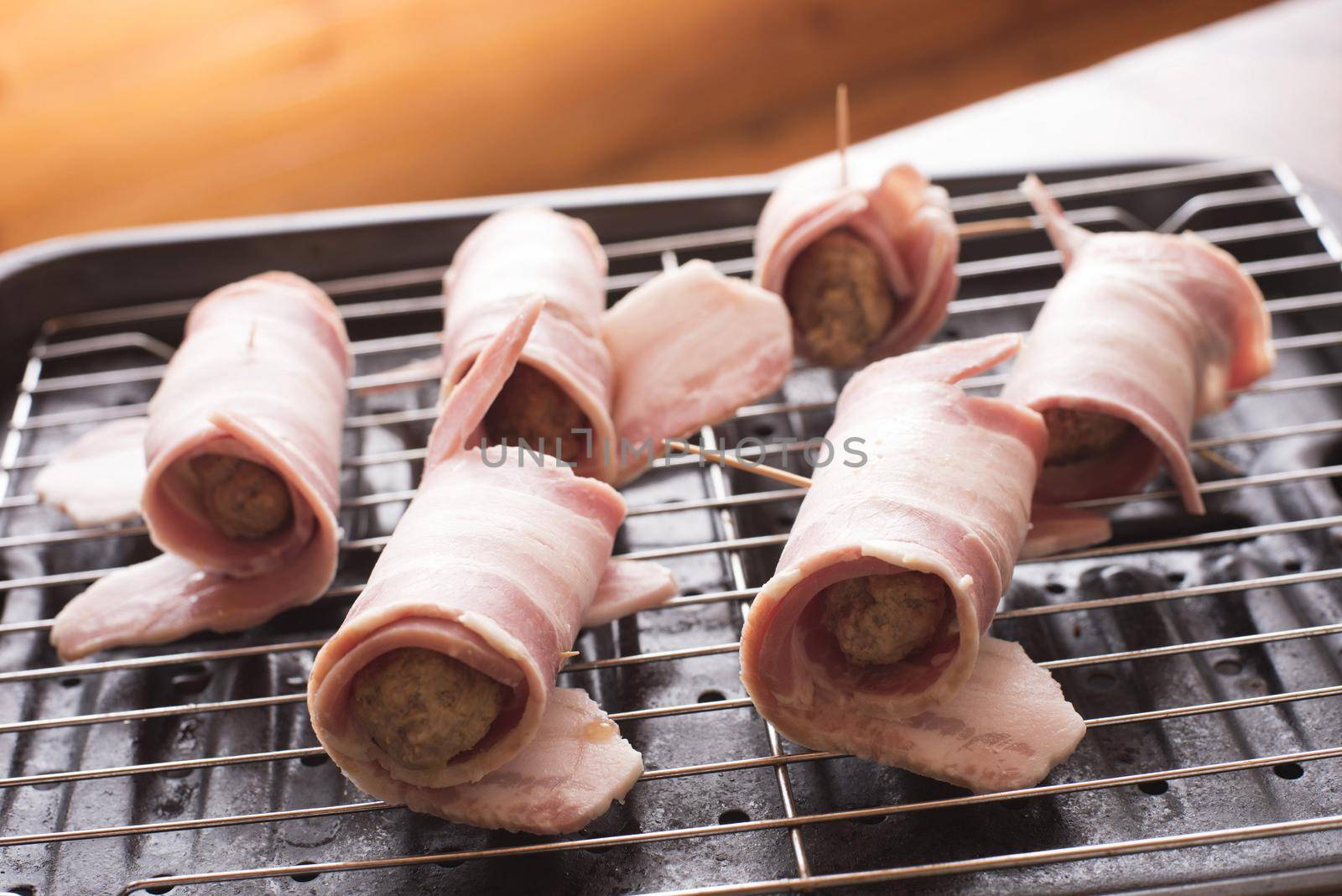 Preparing pigs in blankets on a wire rack with cured ham around pork sausages waiting to be grilled or oven baked