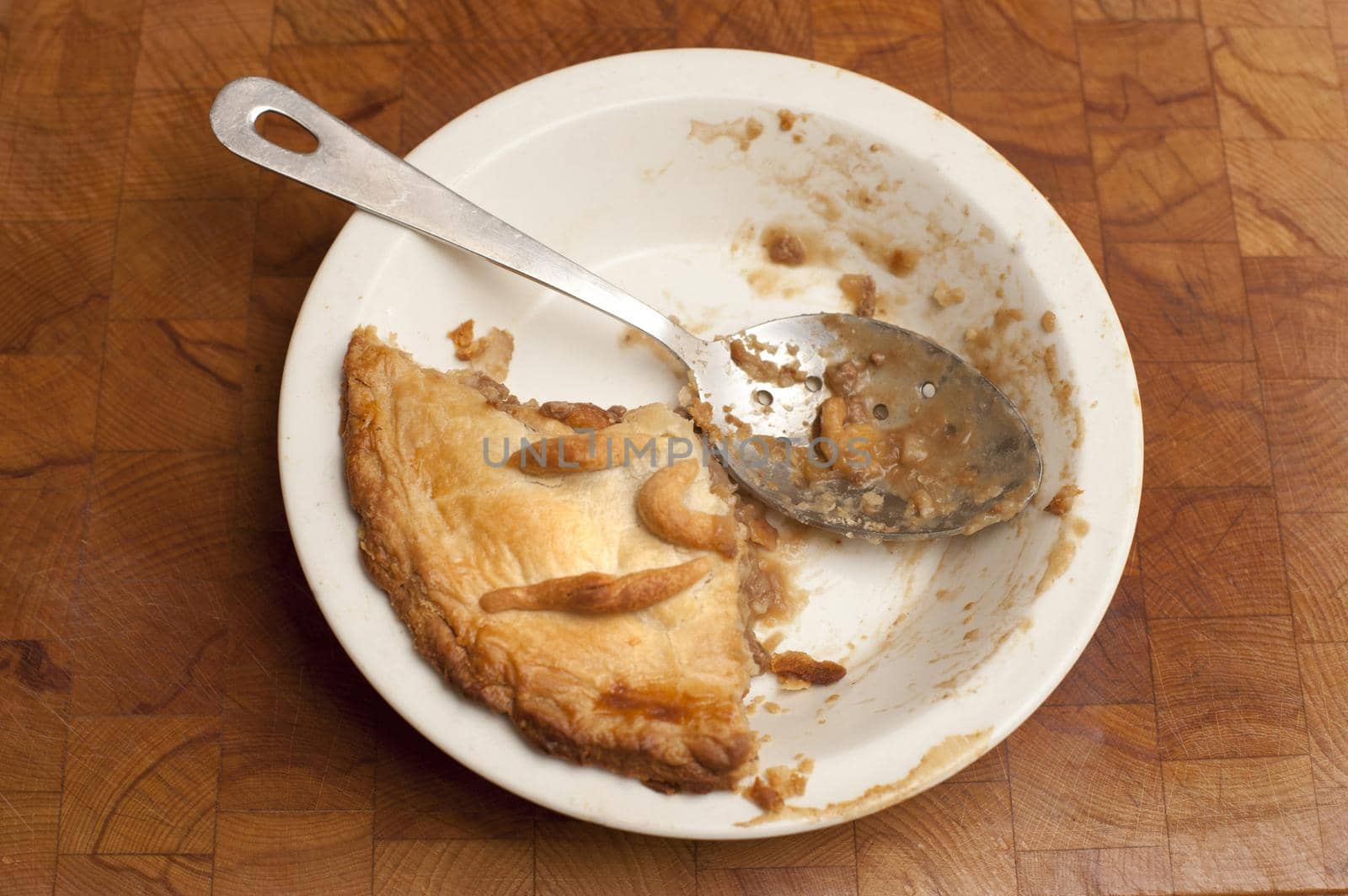 Half eaten freshly baked homemade pie with a pastry crust in a white ceramic oven dish with a messy serving spoon, high angle view