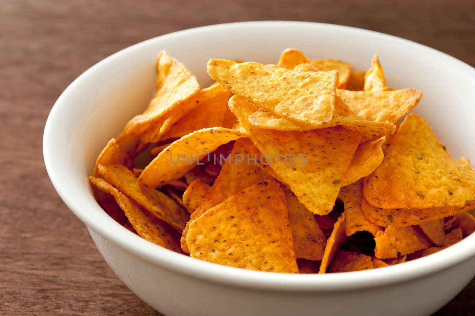 White round bowl full of yellow corn tortilla chips over dark brown wooden table