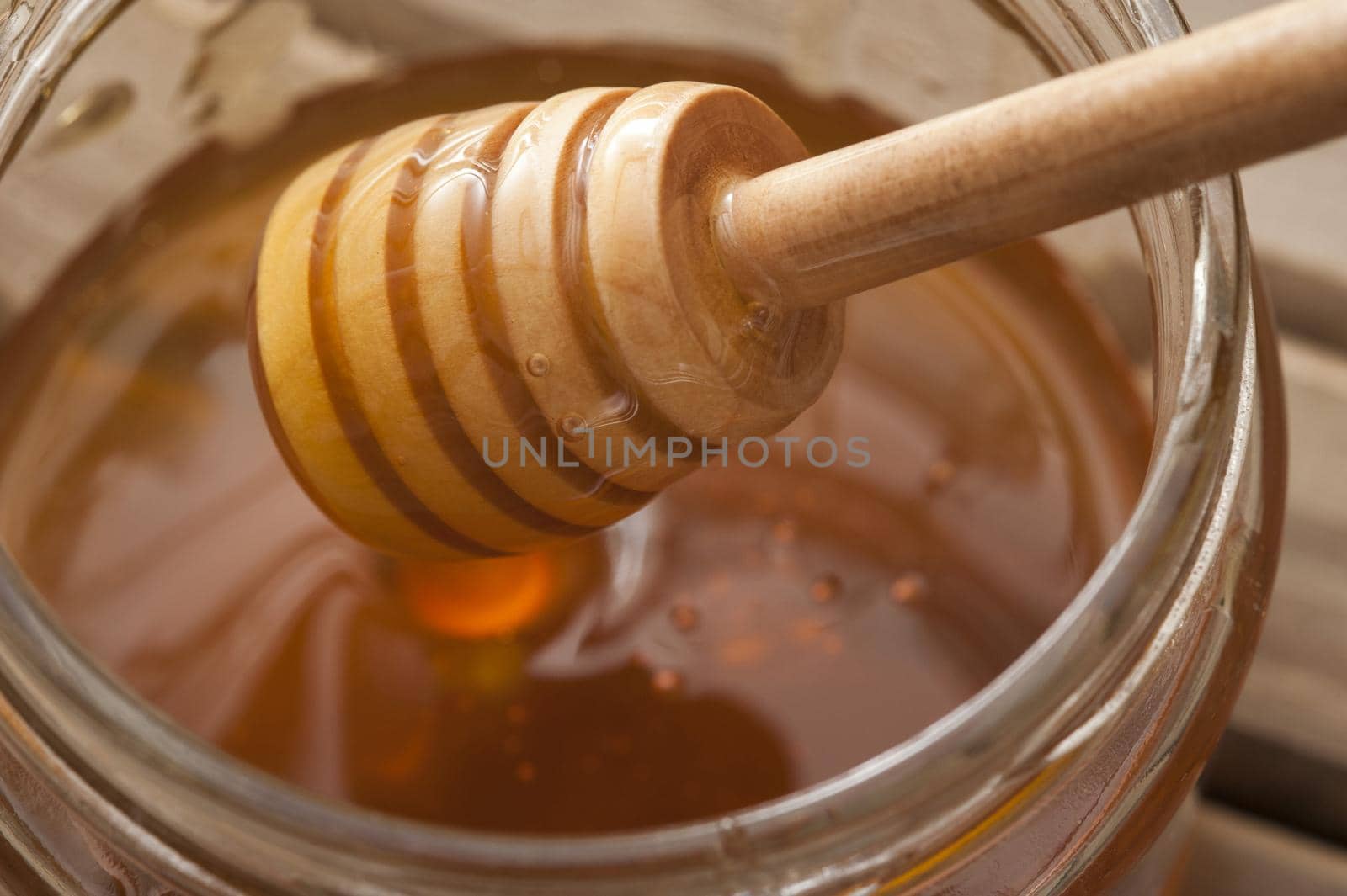 Close up of ribbed wooden dipper in large glass jar filled up with sweet yellow honey